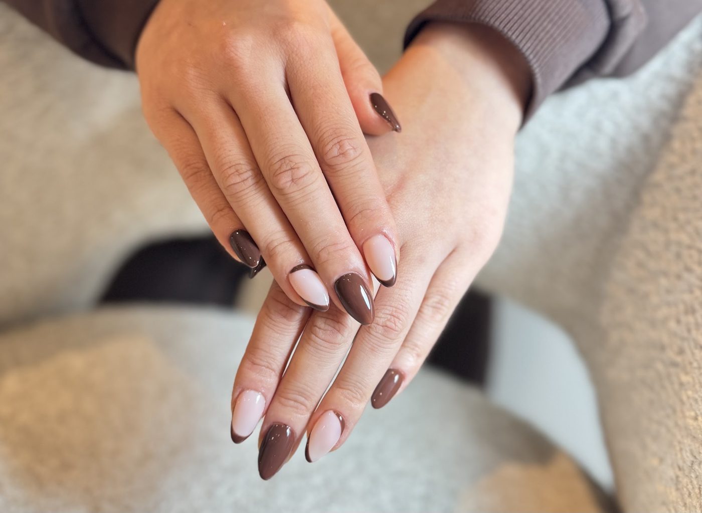 Nude en bruine amandelnagels met designs, twee handen over elkaar